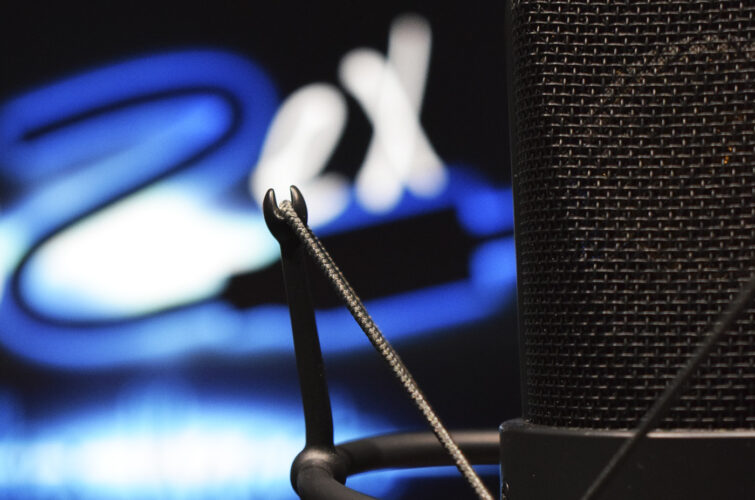 micrófono de condensador neumann tlm 103 frente a monitor con el logo de vozex homestudio